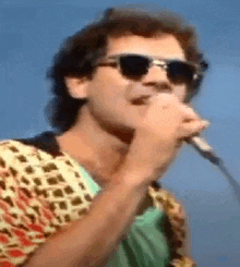 a man singing into a microphone wearing sunglasses and a colorful shirt