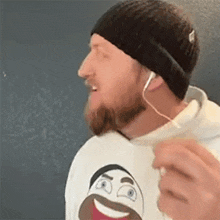 a man with a beard wearing headphones and a beanie is singing .