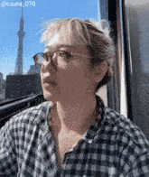 a woman wearing glasses and a plaid shirt looks out the window