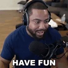 a man wearing headphones and a blue shirt is sitting in front of a microphone and saying have fun .