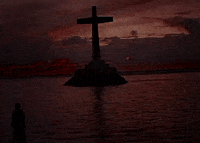 a cross in the middle of a body of water with a sunset in the background