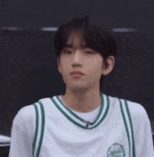 a young man wearing a white and green basketball jersey is standing in front of a black wall .