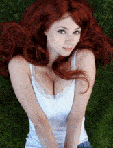 a woman with red hair and a white tank top is laying on the grass