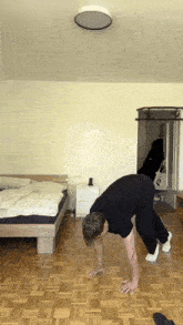 a man doing a handstand in a bedroom with a bed in the background