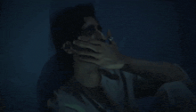 a man is covering his face with his hand in the dark .