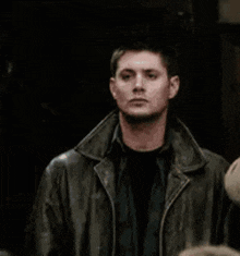 a man in a leather jacket is standing next to another man in a dark room .