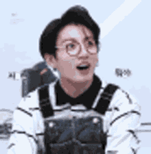 a young man wearing glasses and overalls is sitting in a chair .