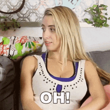 a blonde woman is sitting on a couch with the word oh written on her chest