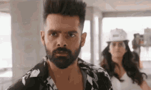 a man with a beard and a woman in a hard hat are standing next to each other in a building .