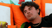 a man with curly hair and a gold chain is laying on an orange couch