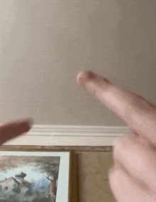 a person 's fingers are pointing at a picture on a wall