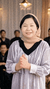 a woman wearing a hijab and a white shirt is smiling with her hands folded