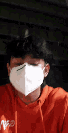 a man wearing an orange hoodie and a white face mask looks at the camera