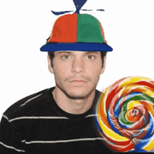 a man wearing a colorful hat holds a large lollipop