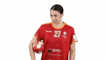 a woman in a red jersey is holding a handball in her hand .