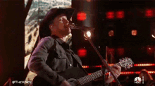 a man singing into a microphone while playing a guitar with the words #thevoice on the bottom