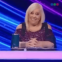 a woman in a sequined top is sitting at a table with her hands folded