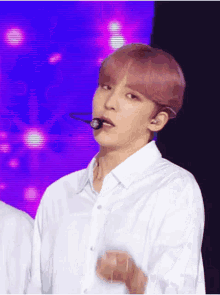 a man with pink hair is wearing a white shirt and holding a microphone in his mouth .