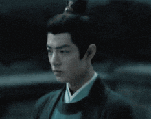 a man with a bun on his head is wearing a black jacket and a blue shirt