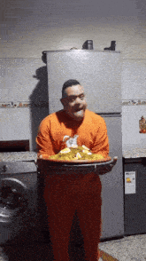 a man in an orange shirt is holding a tray of food in front of a refrigerator
