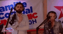 a man and a woman are singing into microphones in front of a sign that says ic dh .