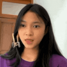 a girl with long black hair wearing a purple shirt and earrings