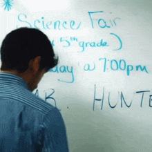 a man stands in front of a white board that says science fair on it