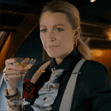 a woman wearing a black shirt and suspenders holds a martini glass