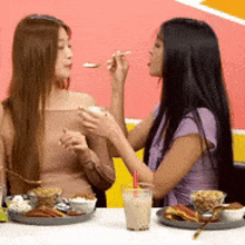 two women are sitting at a table with food and drinks