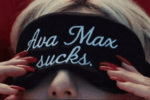 a woman with long red nails wears a black eye mask that says ava max sucks