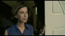 a woman in a blue shirt stands in front of a door
