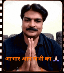 a man with a mustache holds his hands together in front of a sign that says ' abhaar ' on it