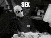 a man with a mask on his face is sitting at a table with the word sex written above him