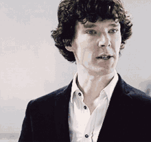 a man with curly hair wearing a black jacket and white shirt