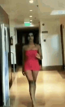 a woman in a red dress is walking in a hallway