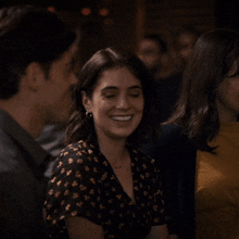 a woman in a black and gold floral shirt smiles while sitting next to a man