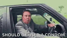 a man in a suit and tie is driving a car while holding a condom .