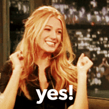 a woman with blonde hair is smiling and holding her fist up in the air with the words yes behind her