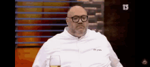 a bald man wearing glasses and a white shirt is sitting in front of a television .