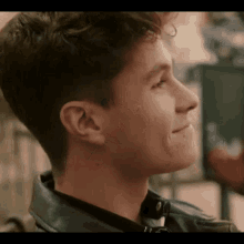 a young man is wearing a leather jacket and smiling .