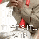 a man in a suit and tie is sitting on a bed and using a cell phone .