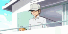 a man in a baseball cap is standing on a balcony holding a box .