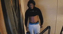 a man wearing headphones and a crop top is standing in a room .