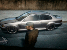 a man wearing a baseball cap stands in front of a silver car