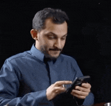 a man in a blue shirt is looking at his cell phone .