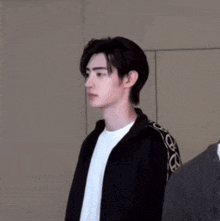 a young man wearing a black jacket and a white t-shirt is standing next to another man .