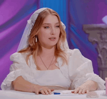a woman in a wedding dress is sitting at a table