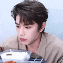 a young man is sitting at a table with a tray of food .