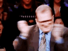 a bald man in a suit and tie is dancing in front of a crowd .