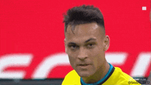 a soccer player wearing a yellow shirt is looking at the camera with a red background